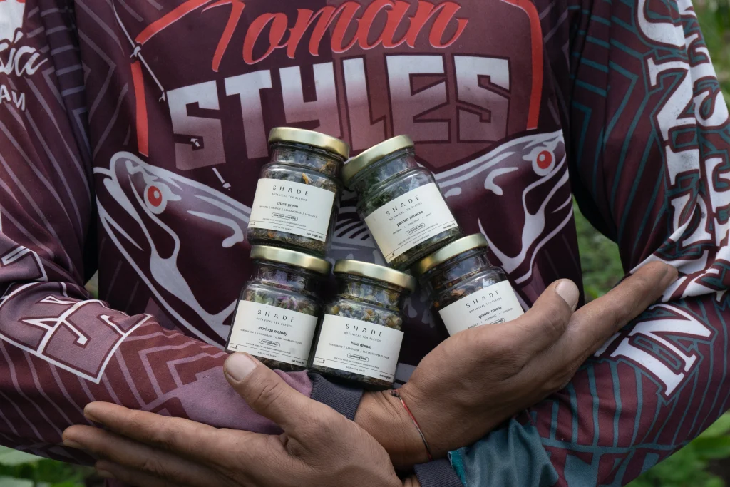 SHADE_Botanicals_-_Loose_Leaf_Tea_Blends_-_Drinking_Lifetyle_-_Farmer_at_Tea_Garden_Holding_70_mL_Recycled_Glass_Jar_-_Complete_Variant